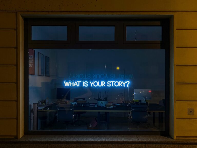 Neon sign in a window says "What's your story?" Image by Etienne Girardet